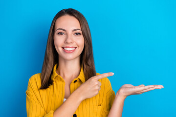 Poster - Photo of nice young brunette lady point hold empty space wear yellow shirt isolated on blue color background