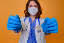 A Doctor In A Blue Uniform With Handcuffs On His Hands, Close-up. Medic In Shackles, The Concept Of Coronavirus Quarantine In The World
