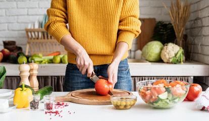 Wall Mural - Front view of female hands making salad cutting tomatoes in the kitchen