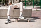 cropped view of african american man sitting on border near skateboard outdoors.
