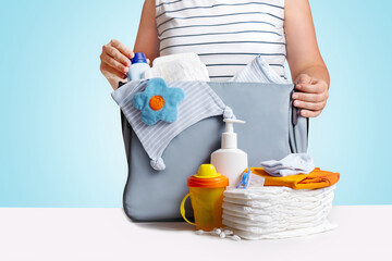 Wall Mural - Woman packing diaper bag on blue background.