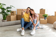 © Prostock-studio - Full length portrait of loving interracial couple sitting on floor among cardboard boxes, showing house key indoors