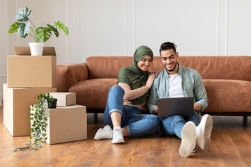 Wall Mural - Happy muslim man and woman using laptop after relocation