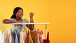 © Prostock-studio - Portrait of young black woman standing near clothing rack, pointing at blank space over orange studio background