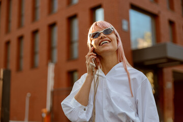 Joyful young woman having phone conversation outdoors