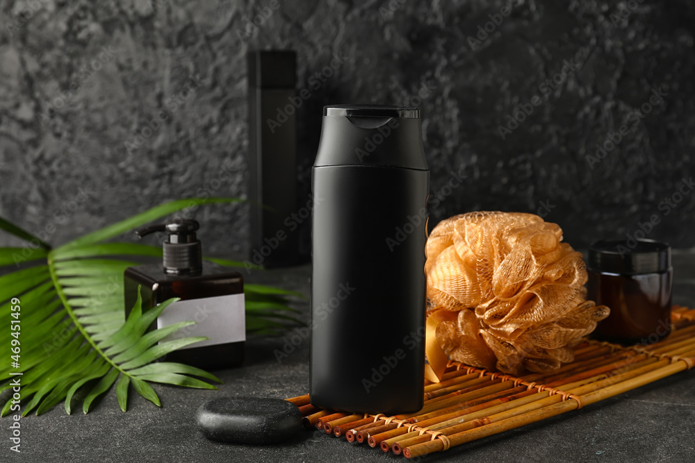 Composition with bottle of shower gel, sponge and palm leaf on dark background