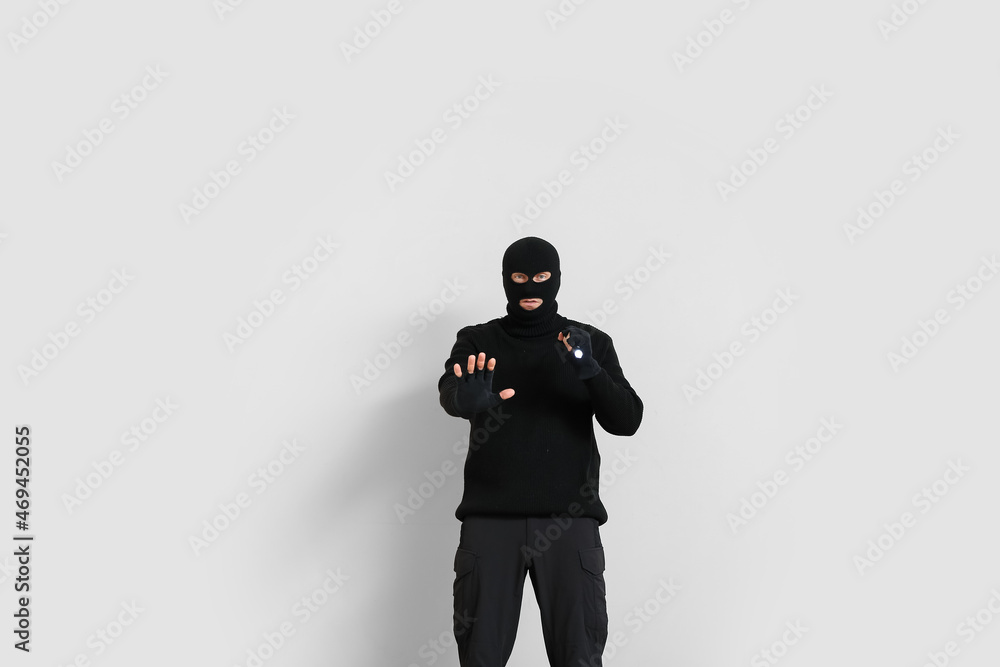 Male criminal with flashlight showing stop gesture on light background