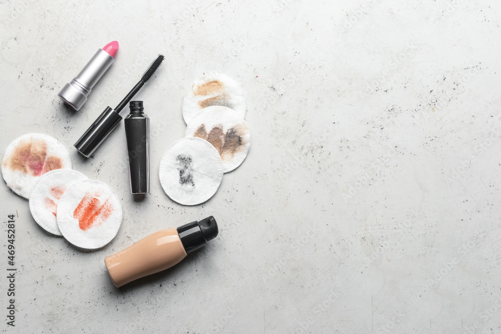 Lipstick, mascara, foundation and used cotton pads on light background