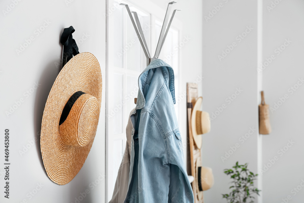 Wicker hat and hanger with jackets near white wall in hallway, closeup