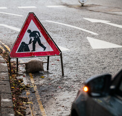 Traffic signs. A sign indicating a construction road work in progress on a street. Car in foreground standing with the light on.