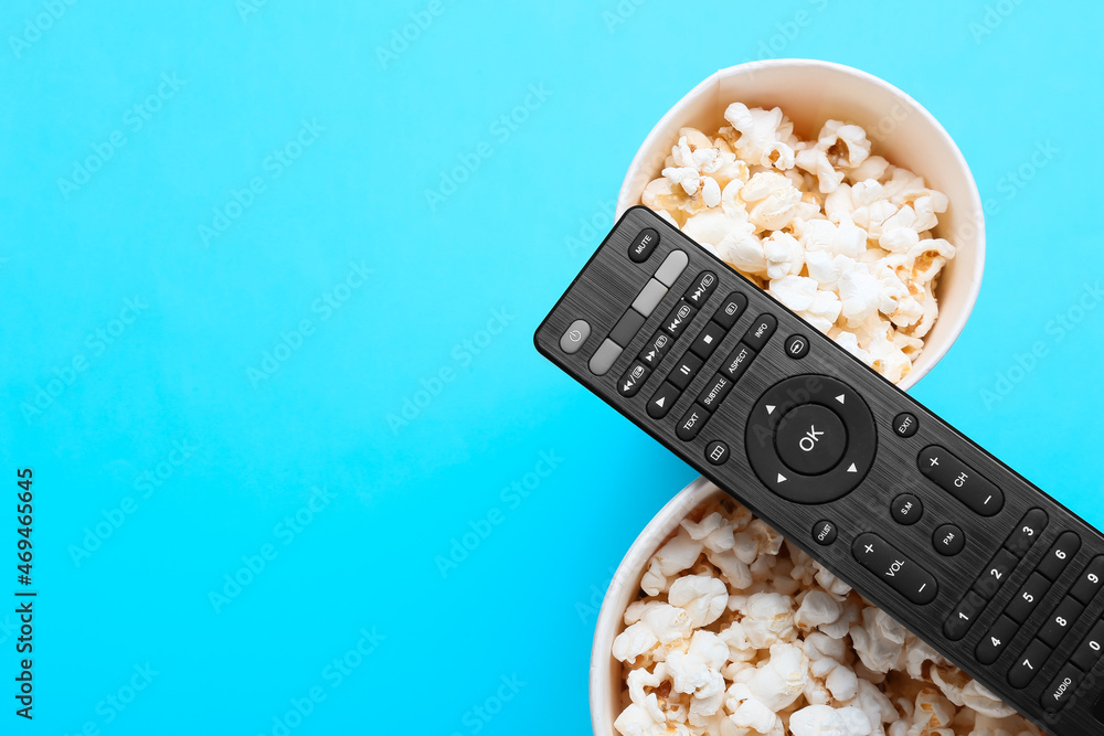 Modern TV remote control and buckets with popcorn on color background