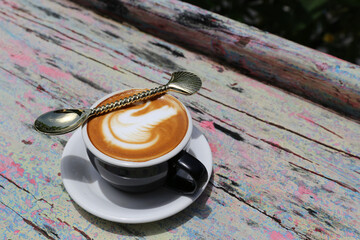 cup of tasty cappuccino with latte art and golden spoon on wooden table background