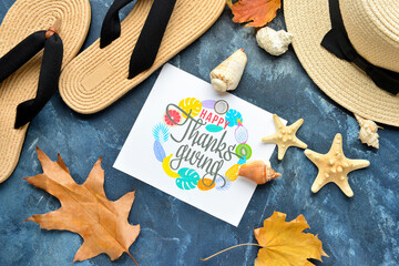 Flip flops, wicker hat, seashells, dry leaves and paper card with text HAPPY THANKSGIVING on color background