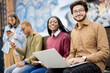 © rh2010 - Portrait of multiracial students sitting together with laptop on wooden bench outdoors. Concept of remote and e-learning. Idea of students lifestyle. Young guys and girls at university campus
