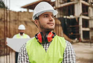 Smiling young male contractor standing at construction site and looking away