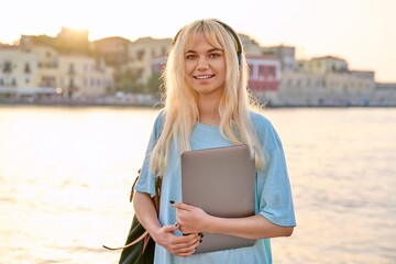 Wall Mural - Outdoor portrait of female student teenager in headphones with backpack and laptop