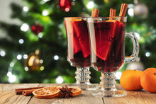 Two Glass Of Christmas Mulled Wine Or Gluhwein With Spices And Orange Slices On Rustic Table Against The Christmas Tree. Traditional Drink On Winter Holiday