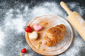 Wall Mural - Fresh baked butter crushed nuts breakfast croissant, french heart macarons, strawberry and crumbs  on wooden board