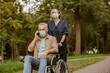 © Kostiantyn - Young nurse in face shield and protective face mask taking care of senior handicapped patient in wheelchair talking on the phone during a walk in the park