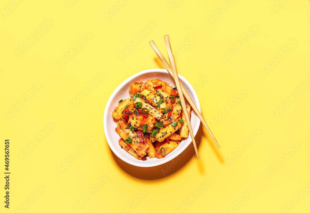 Bowl with honey chilli potato and chopsticks on color background