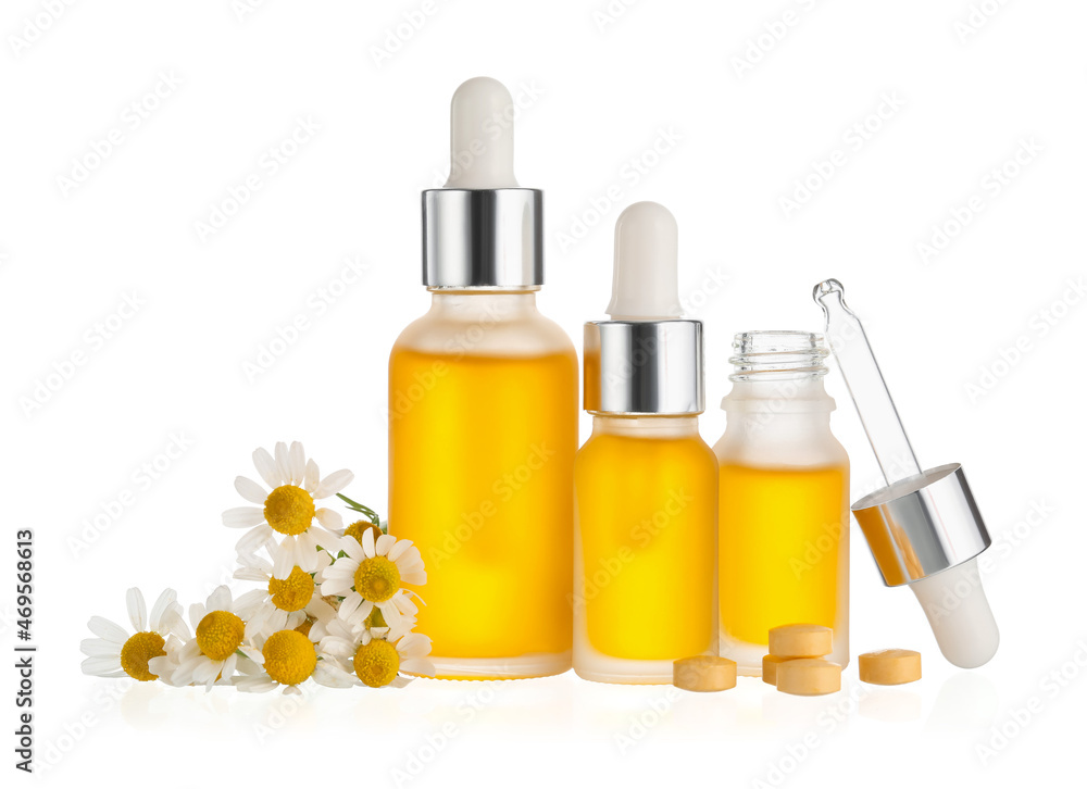 Different bottles of essential oil and chamomile flowers on white background