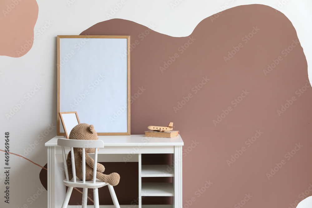 Table with wooden airplane, book and blank frames near color wall