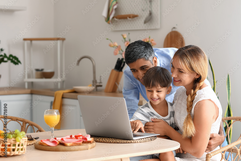 Happy parents with their little son using laptop at table in kitchen