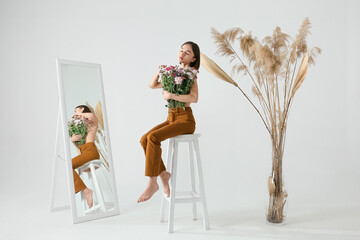 Sticker - Sexy young woman with bouquet of flowers sitting on chair against light background