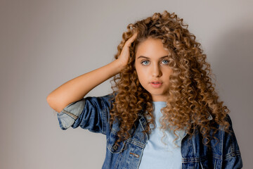 Wall Mural - portrait of a cute smiling blonde girl with blue eyes and curly hair in a denim jacket. young woman with beautiful clean healthy skin. natural make up, spa concept, fashion concept. High quality photo