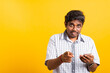 © sorapop - Closeup Asian happy portrait young black man holds a mobile smartphone and pointing finger out to the camera, studio isolated on yellow background