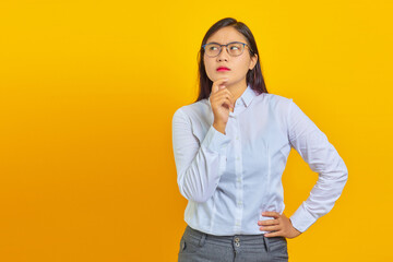 Pensive young beautiful business woman rubs chin and thinking question over yellow background