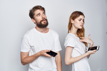 Wall Mural - a young couple in white T-shirts with phones in their hands light background