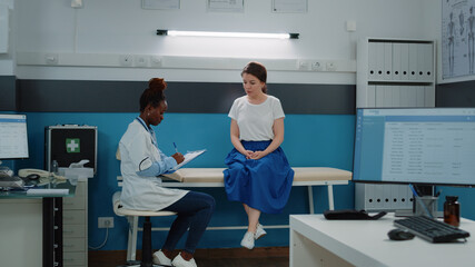 Wall Mural - Young patient on bed talking to doctor for annual checkup visit and examination. Medic with healthcare information consulting woman at medical appointment. Specialist doing consultation