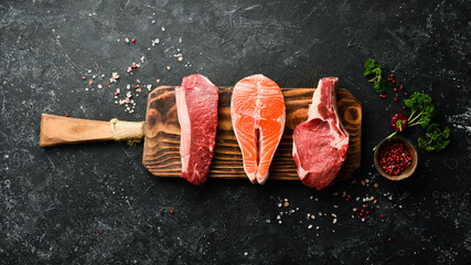 Wall Mural - Mix of steaks: salmon, beef, pork and chicken, on a dark stone background. Top view. Organic food.