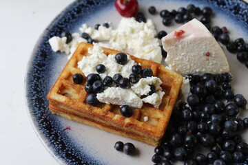 Canvas Print - delicious healthy breakfast. Belgian soft waffles with curd cheese cream and blueberry cherries lie white blue plate view from the top. Delicious still life