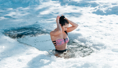 Girl with bikini and a watch in frozen lake ice hole. Woman hardening the body in cold water. Good immunity is protection against many diseases. Vintage color filter