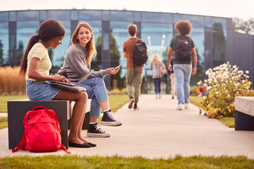 Wall Mural - Female University Or College Students Sitting Outdoors On Campus Talking And Working On Laptop