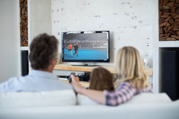 Canvas Print - Rear view of family sitting at home together watching athletics event on tv