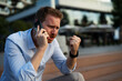 © JustLife - Businessman using the phone while sitting on the stairs. Angry upset man using the phone