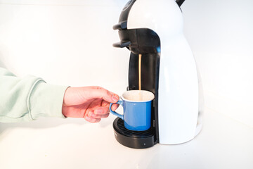 Closed up with a male hand holding a coffee cup under the coffee machine and decorated with coffee capsules.