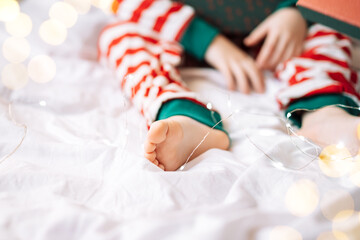 Wall Mural - Child in striped pajamas holding gift box while sitting on white bed with garland