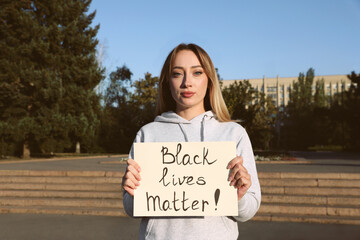 Young woman holding sign with phrase Black Lives Matter outdoors. Racism concept