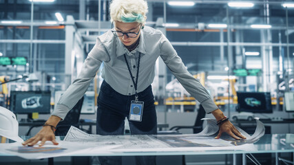 Young Female Engineer Looking at a Technical Blueprint at Work in an Office at Car Assembly Plant. Industrial Specialist Working on Vehicle Parts in Technological Development Facility.