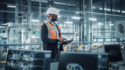 Leinwandbilder - African American Engineer Using Laptop and Looking Out of the Office at a Car Assembly Plant. Vehicle Factory Line Operator Working on Computer, Overviewing Autonomous Electric Car Production.