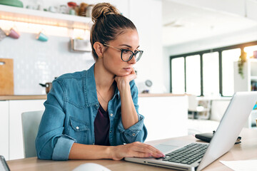 Wall Mural - Pretty young woman working with laptop during morning coffee in the kitchen at home.