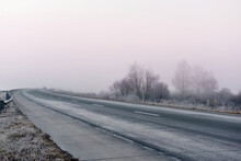 A Road With A Sharp Bend In The Early Morning In Frosty Foggy Weather. Grass, Trees In Frost And Fog Along The Road.
