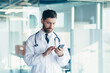 © Liubomir - Male doctor in a white coat in a modern clinic reads information from a mobile phone corresponds with colleagues happy and smiles