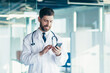 © Liubomir - Male doctor in a white coat in a modern clinic reads information from a mobile phone corresponds with colleagues happy and smiles