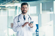 © Liubomir - Male doctor in a white coat in a modern clinic reads information from a mobile phone corresponds with colleagues happy and smiles
