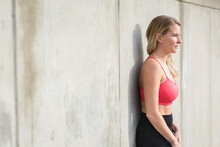 Woman In Workout Gear Relaxes Against Concrete Wall